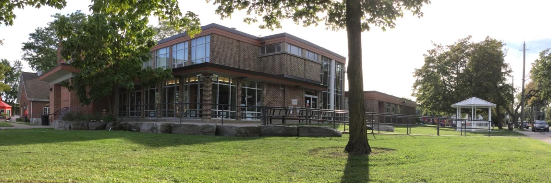 Brick building with large windows, surrounded by trees on a sunny day.